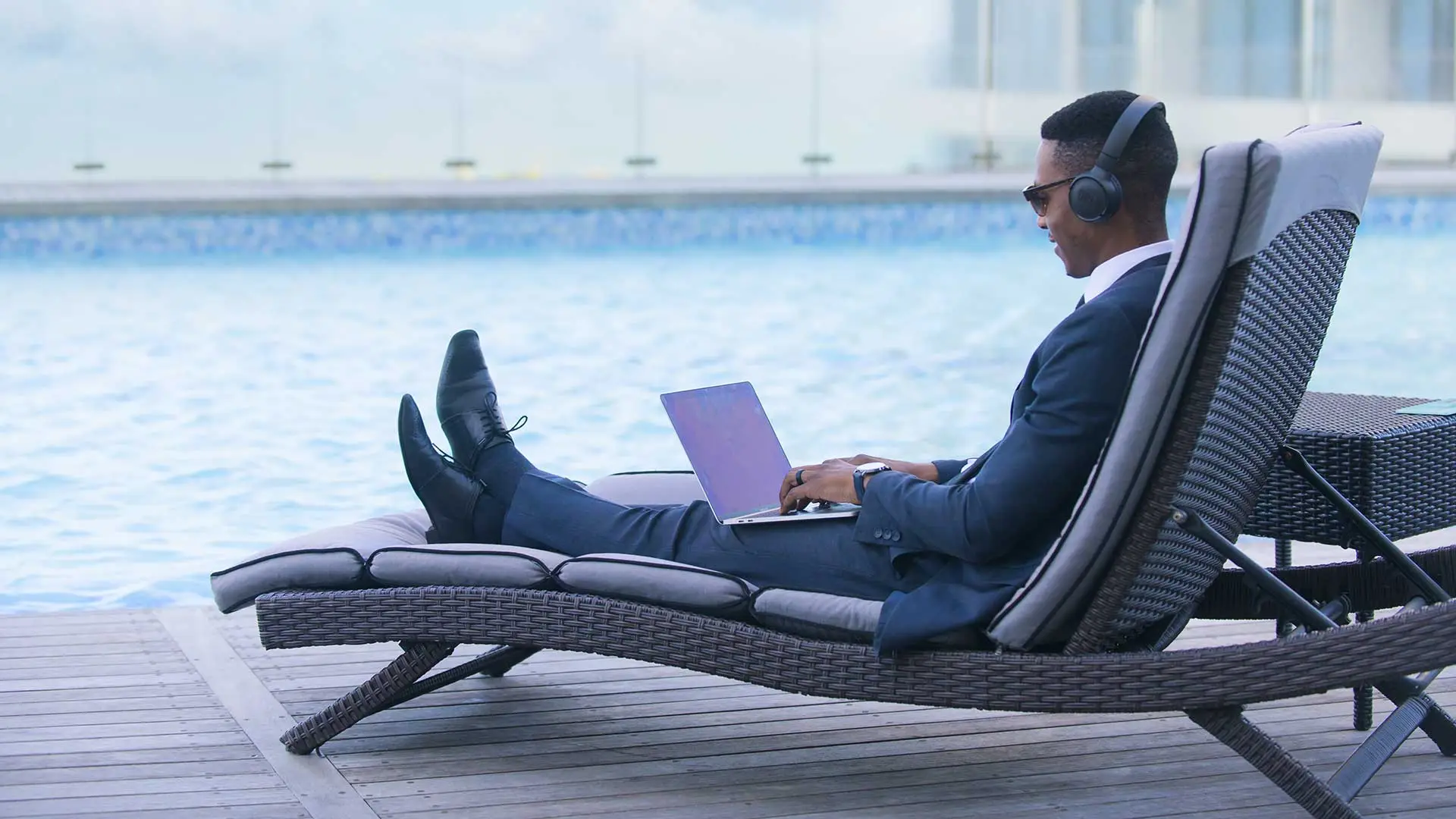 businessman sitting on a chair near the pool working on a laptop