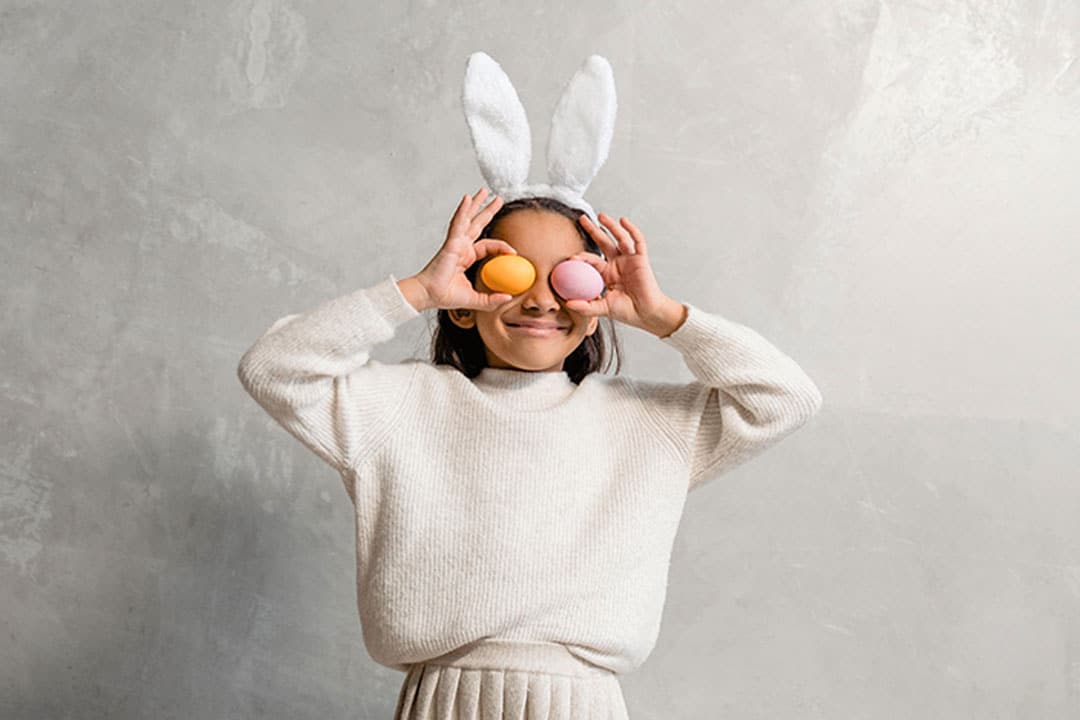 A child with bunny ears that's playing with easter eggs.