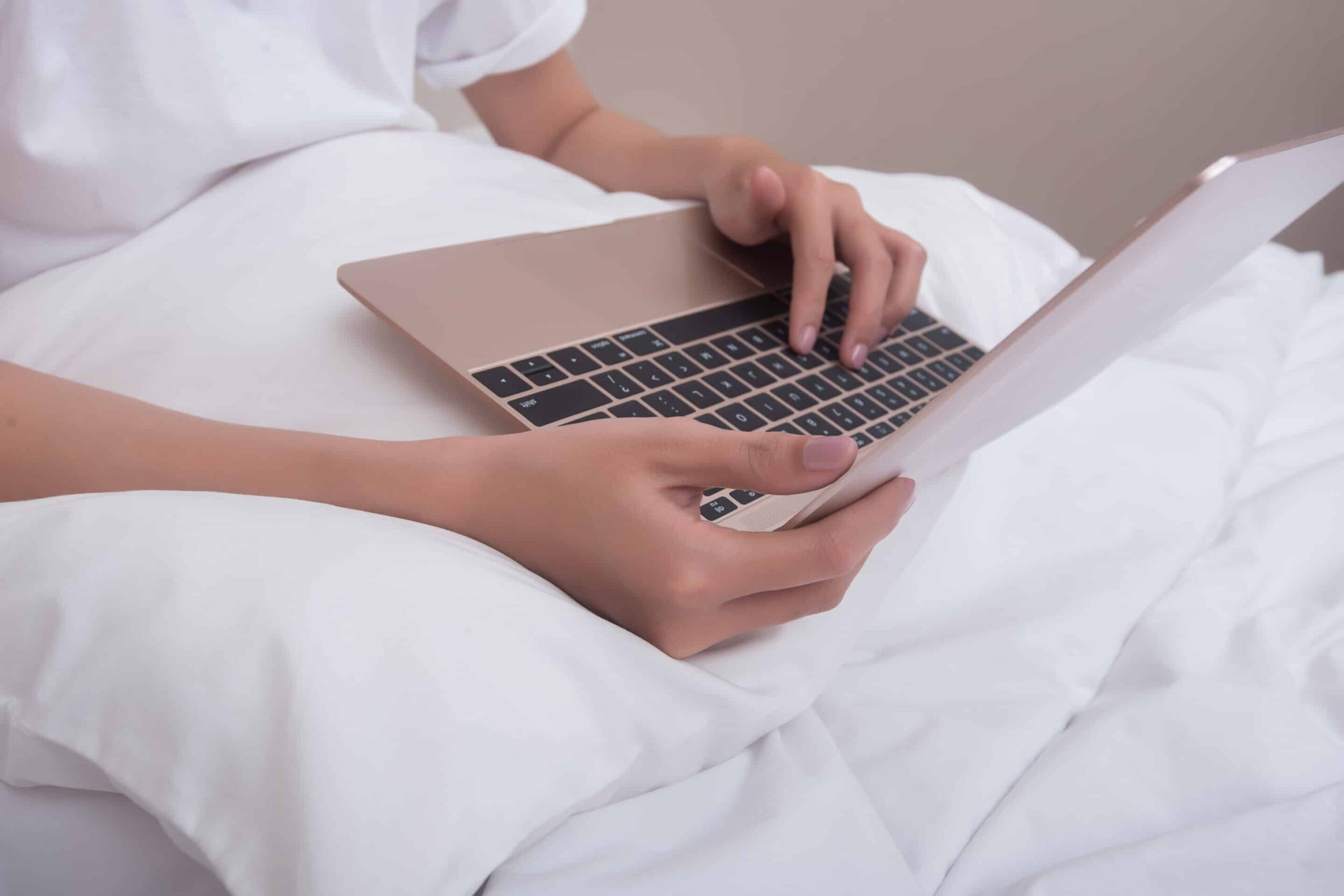 Woman using laptop smiling sitting on bed at home woke up in the