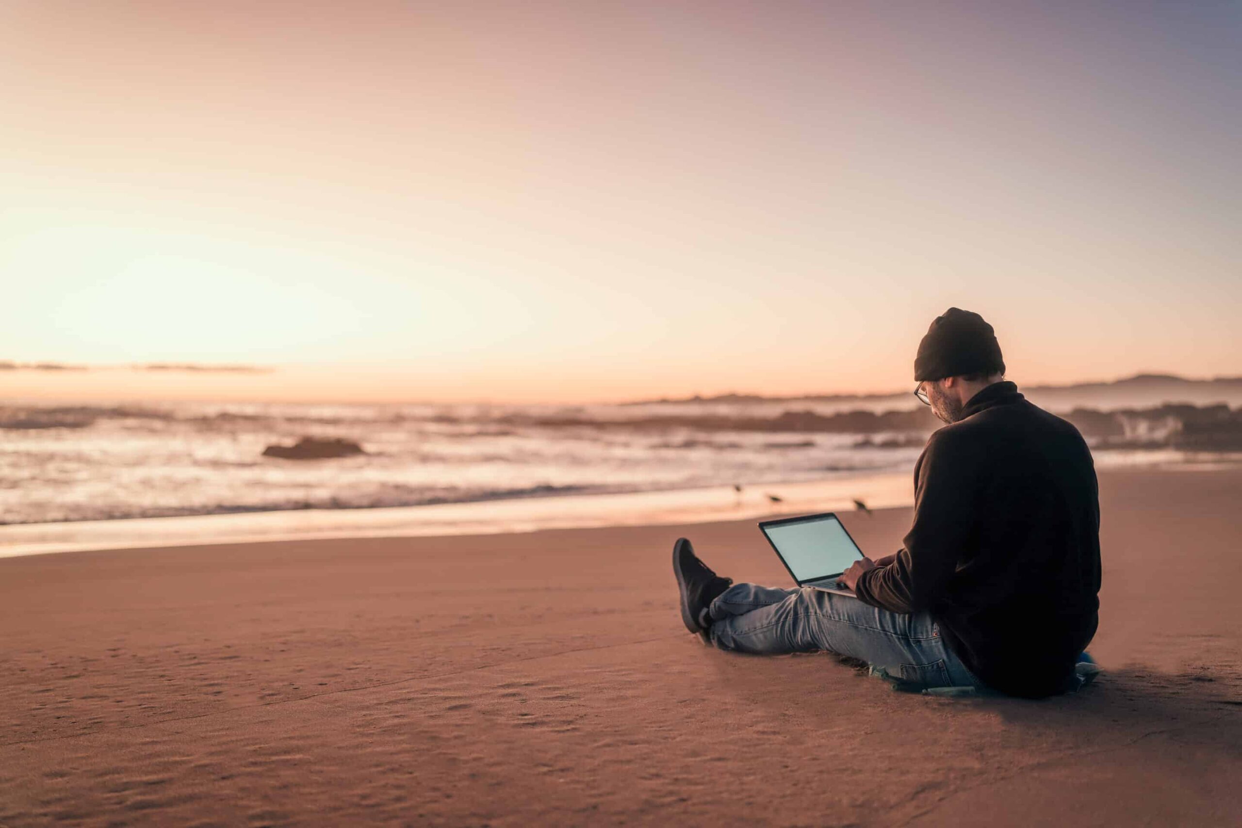 silhouette of a person working on his laptop outdoors on the beach at golden hour, back view working-remotely-cape-town