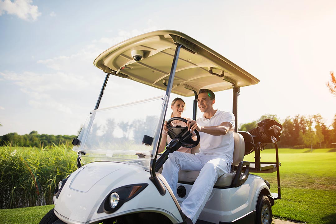 Un couple souriant au volant d'une voiturette de golf, traversant un parcours de golf verdoyant par une journée ensoleillée